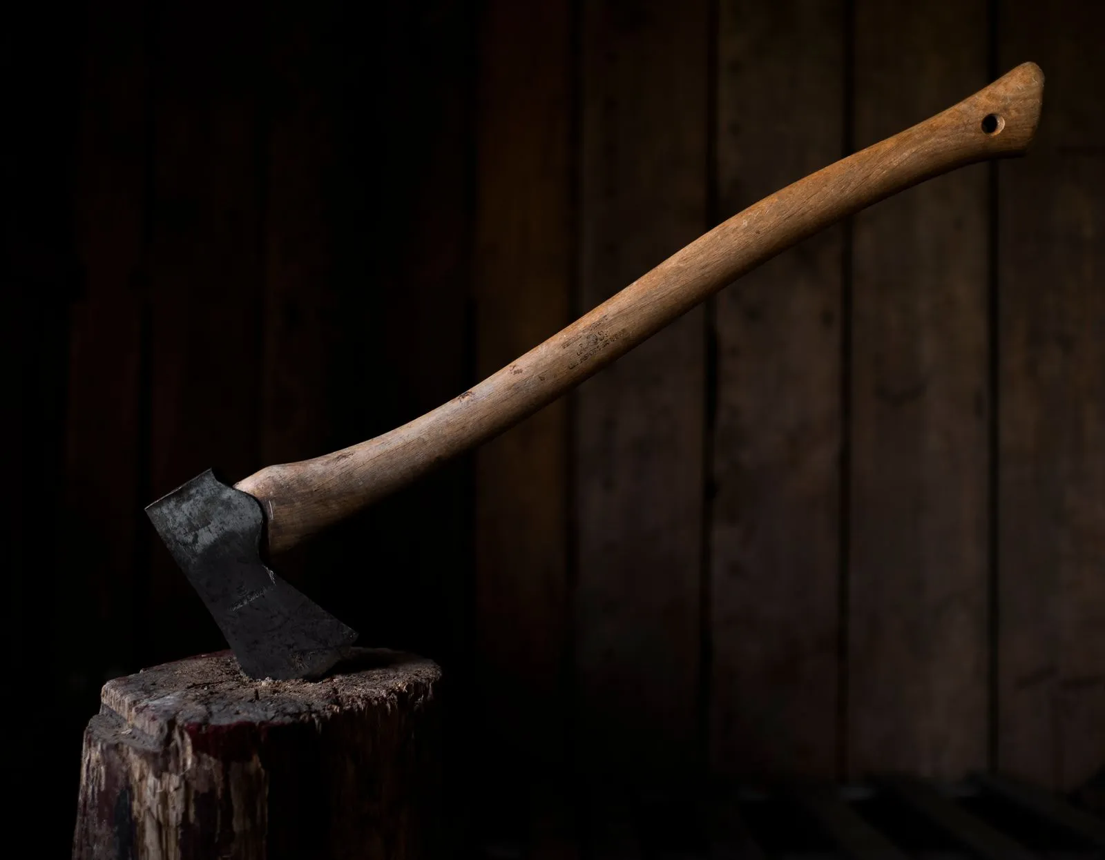 A rustic axe embedded in a log, set against a dark wooden wall, evoking traditional craftsmanship.
